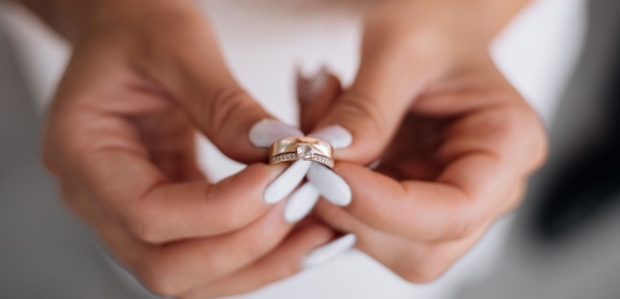 Hands holding a gold ring and engagement ring together