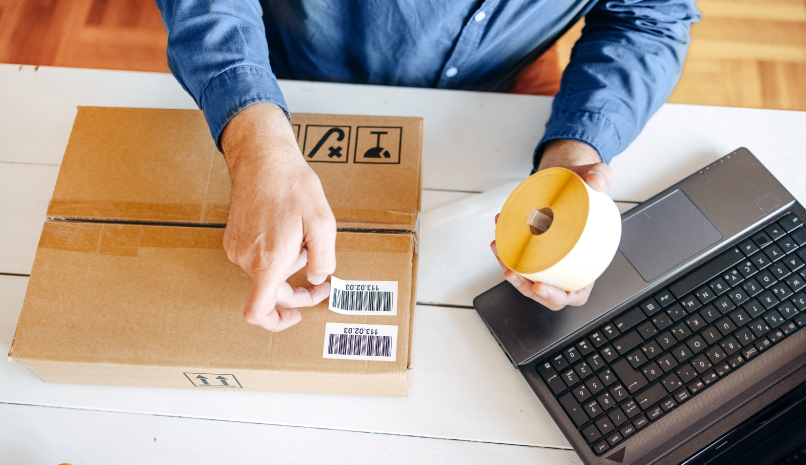 Person with a laptop and taping a shipping label on a box