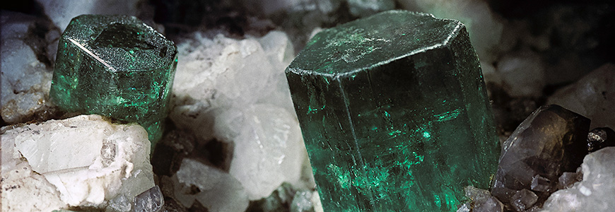 multiple emerald gemstones sit in much larger rock formation