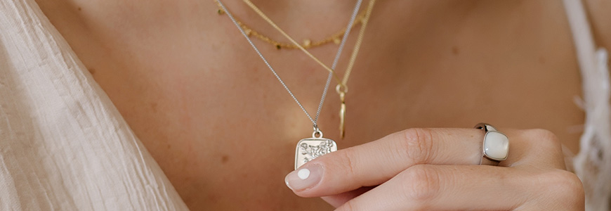 woman holds pendant necklace while wearing additional layered necklaces and large ring