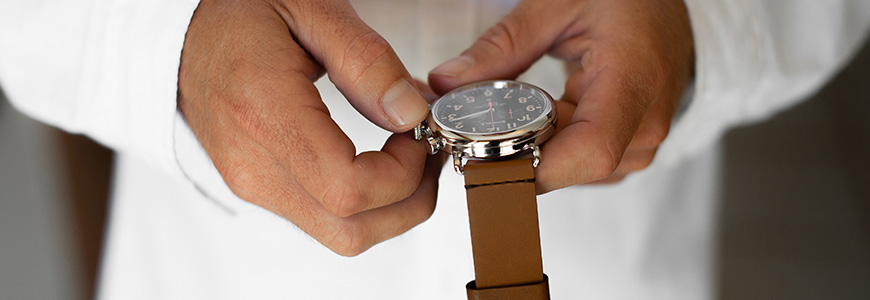 man in white shirt adjusts watch with brown leather strap 