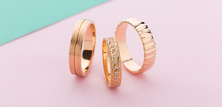 set of three rose gold rings on a pink background