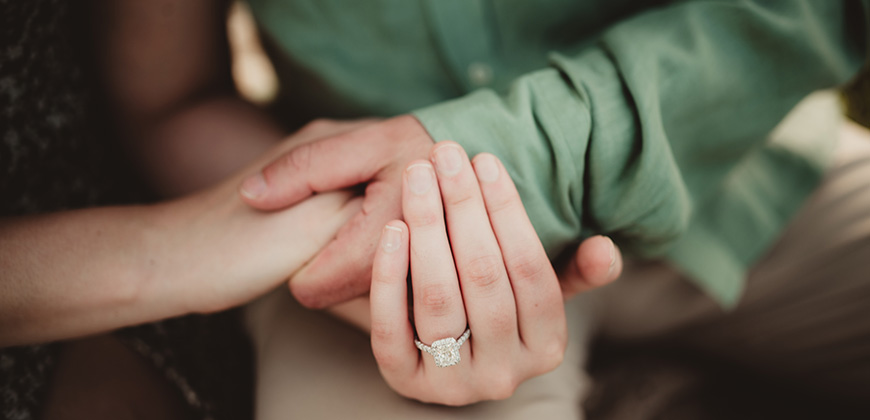 man in green shirt holds woman wearing an engagement ring's hand