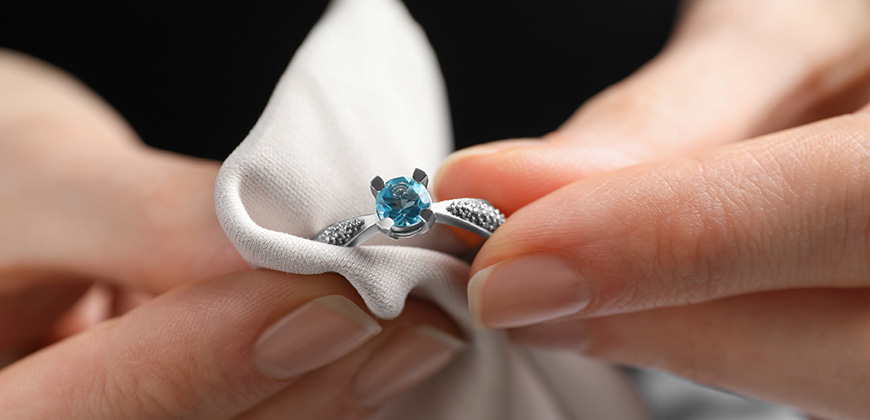 person cleaning white gold and topaz ring with microfiber cloth
