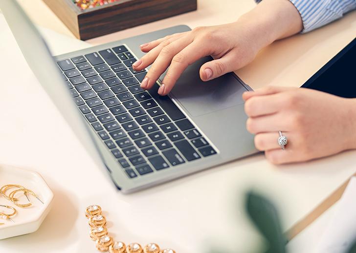 Person typing on a laptop with jewelry around them