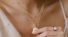woman holds pendant necklace while wearing additional layered necklaces and large ring