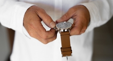 man in white shirt adjusts watch with brown leather strap 