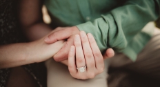 man in green shirt holds woman wearing an engagement ring's hand