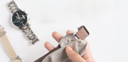 A hand cleaning a watch with a cloth and two other watches in the background